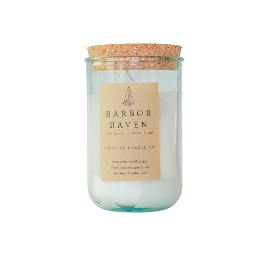 Clear glass jar candle with white wax and a natural cork lid. The tan paper label features a sailboat illustration and reads 'HARBOR HAVEN', 'white lavender | cotton | sage', and 'UNSALTED CANDLE CO.' on a white background.