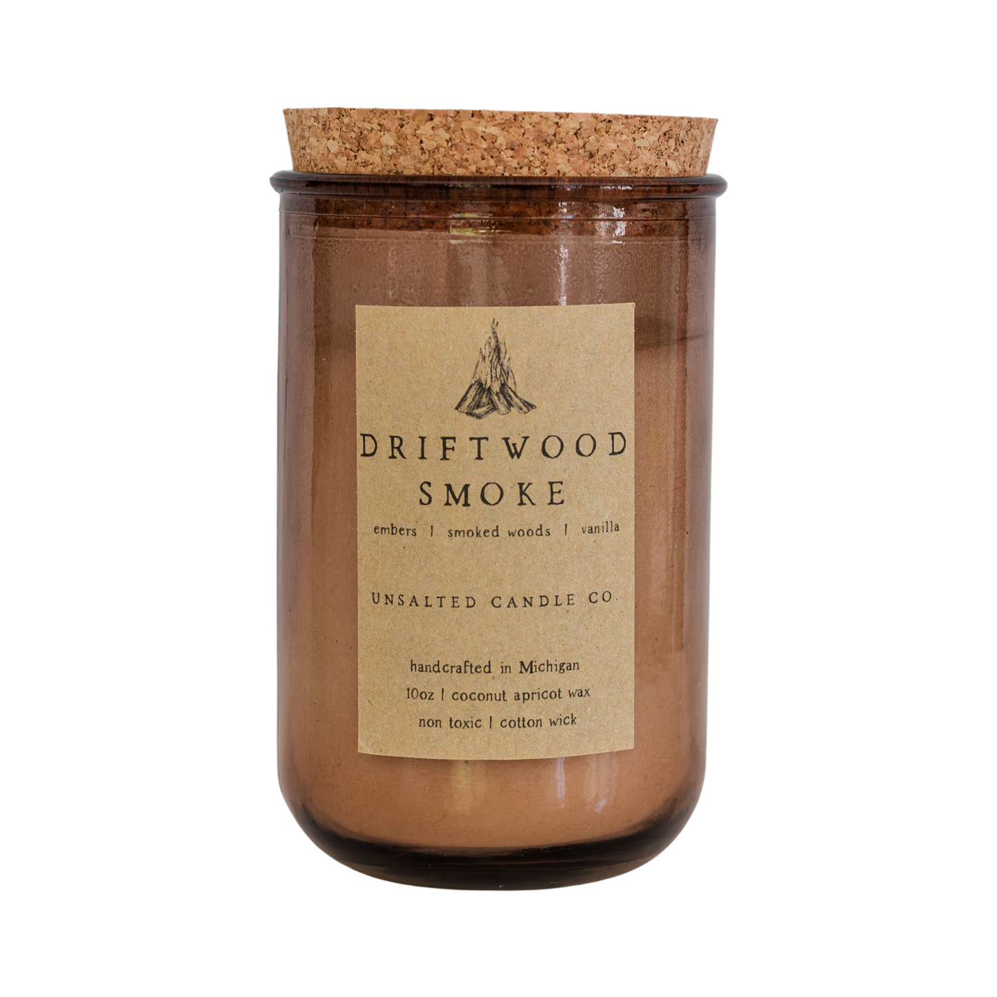 A Driftwood Smoke scented unsalted candle in an amber glass jar with a cork lid, featuring a beige paper label with a black campfire logo and text.