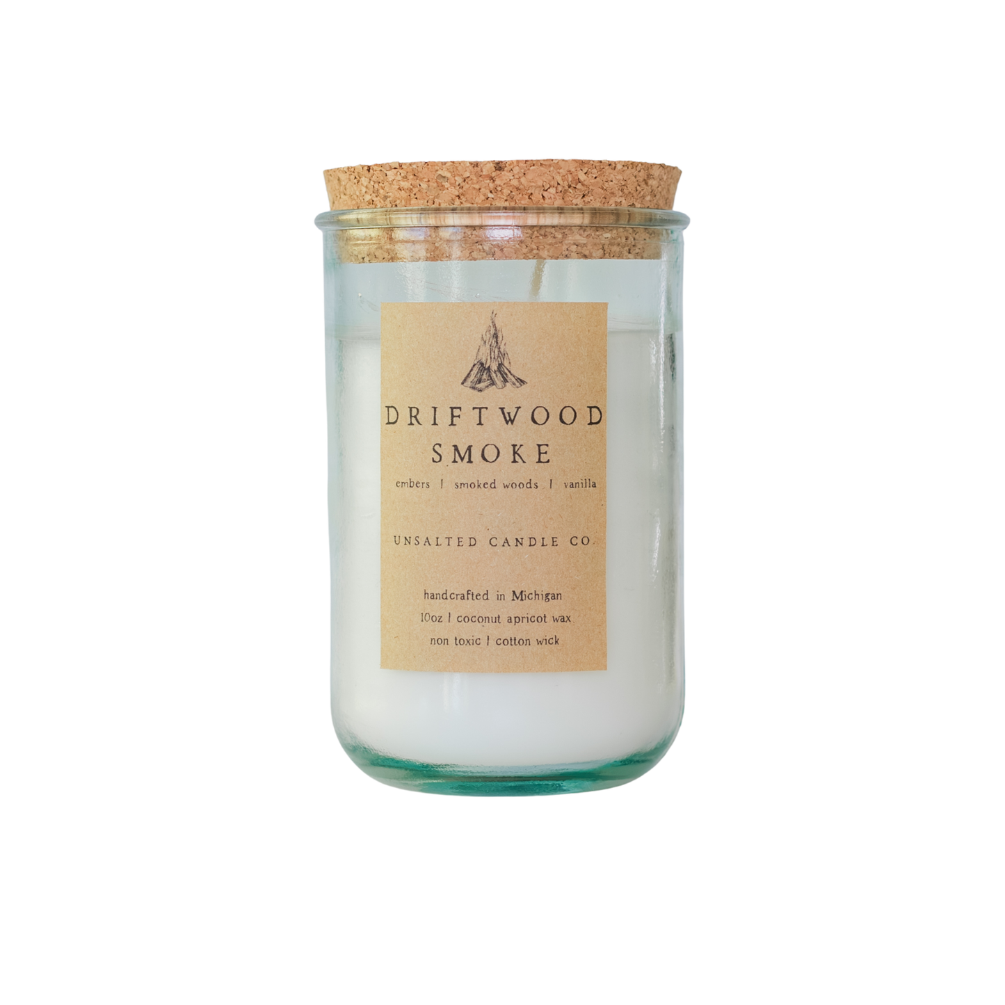 Clear glass jar candle with white wax and a natural cork lid. The tan paper label features a campfire illustration and reads 'DRIFTWOOD SMOKE', 'embers | smoked woods | vanilla', and 'UNSALTED CANDLE CO.' on a white background.