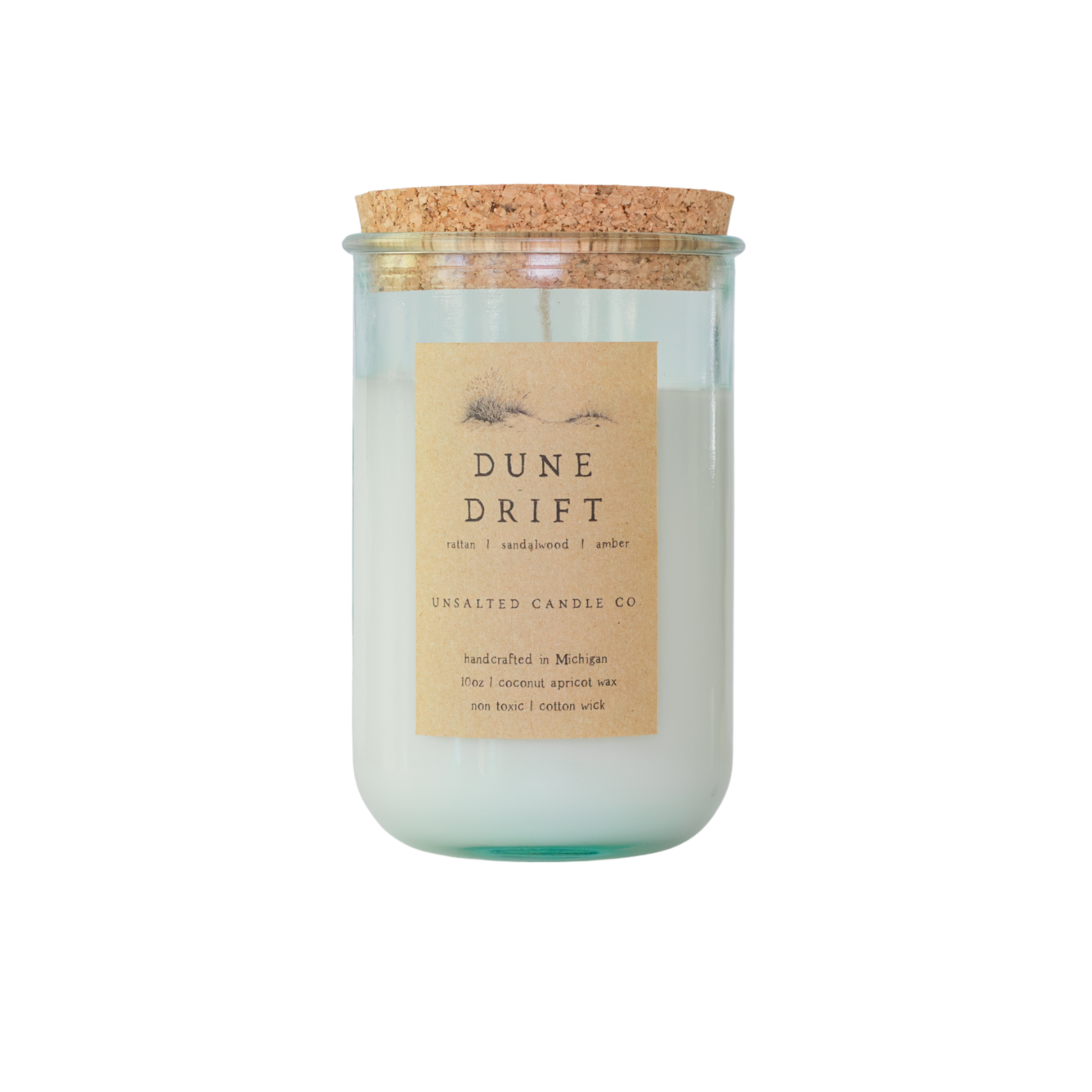 Clear glass jar candle with white wax and a natural cork lid. The tan paper label features a sand dune illustration and reads 'DUNE DRIFT', 'rattan | sandalwood | amber', and 'UNSALTED CANDLE CO.' on a white background.