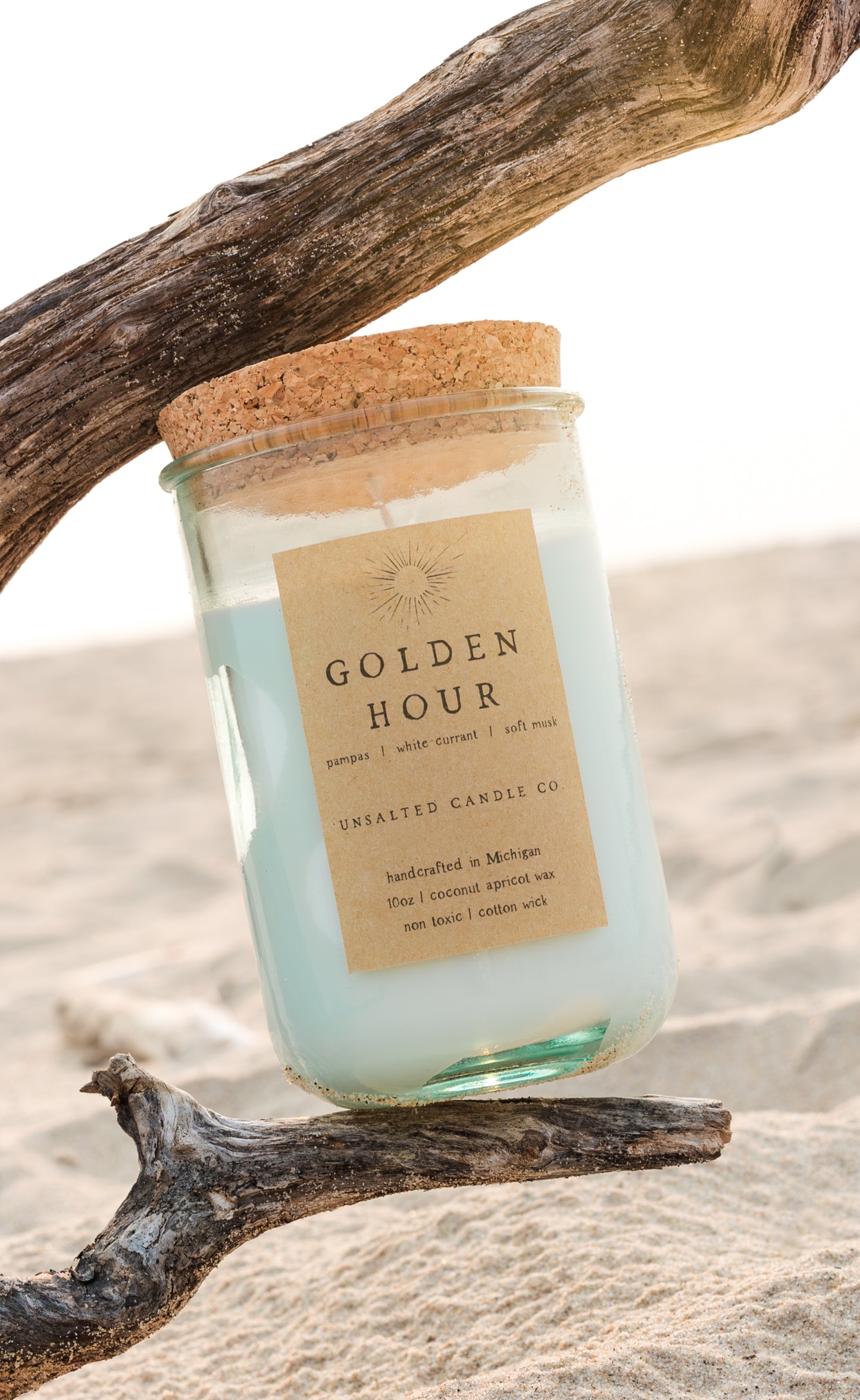 Golden Hour candle by Unsalted Candle Co. nestled between driftwood on a sunlit Michigan sand dune.