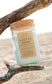 Golden Hour candle by Unsalted Candle Co. nestled between driftwood on a sunlit Michigan sand dune.