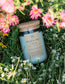 Morning Veil floral candle by Unsalted Candle Co. nestled in green meadow grass surrounded by pink wildflowers and delicate white daisies.