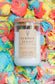 A glass jar candle with a cork lid and a kraft paper label reading 'SUMMER SCOOP' and 'UNSALTED CANDLE CO.' The candle is placed on top of a colorful, textured background resembling melted ice cream swirls in blue, pink, yellow, and orange.